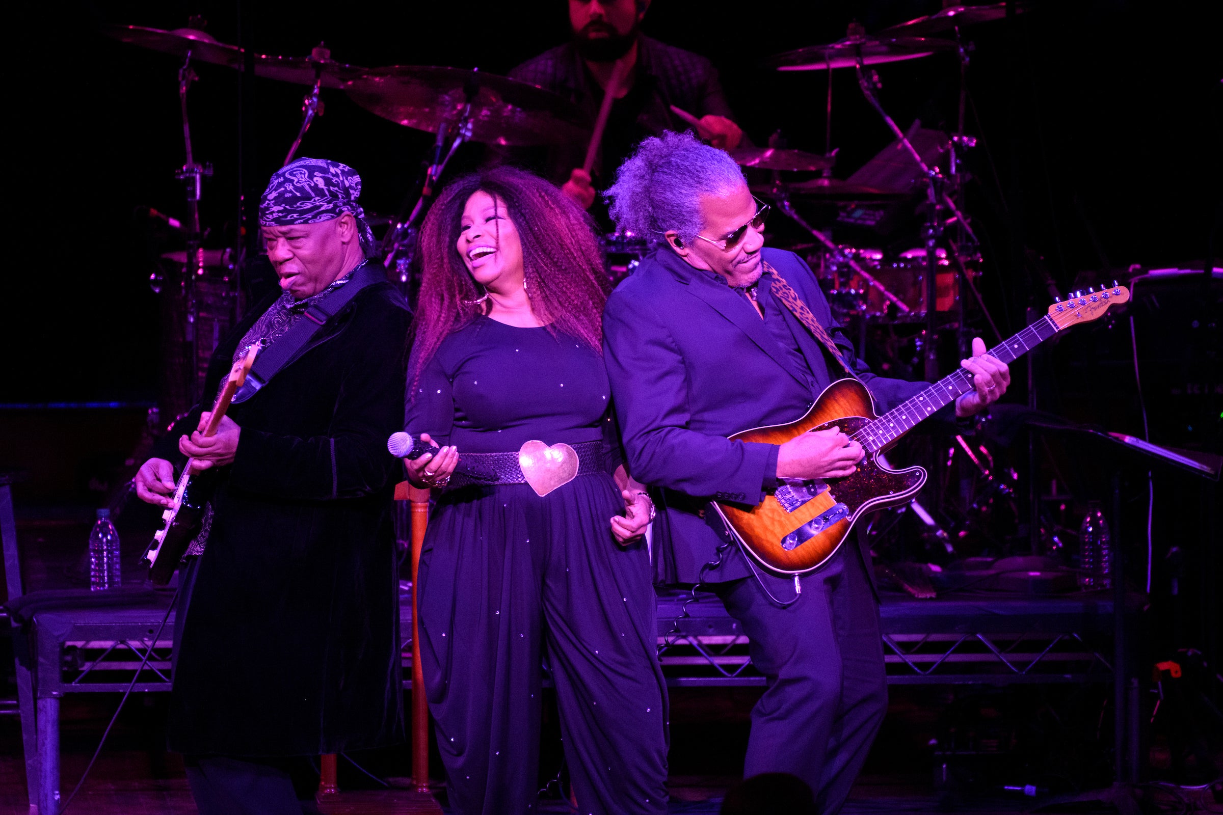 Chaka Khan leans into her guitar and bass players while performing under purple light
