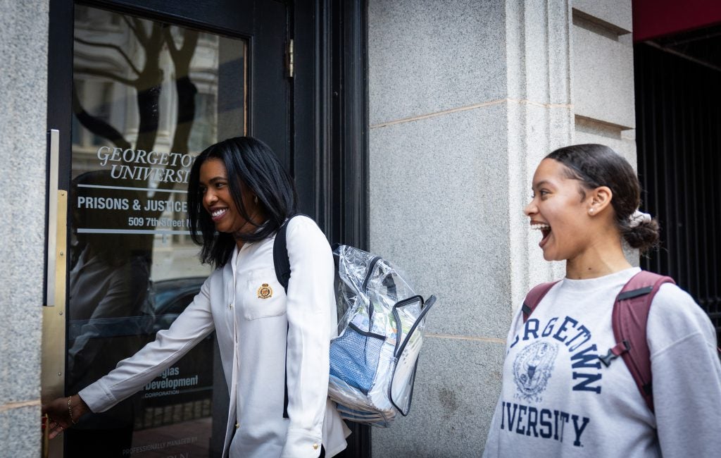 A woman laughs with another woman as she opens a door